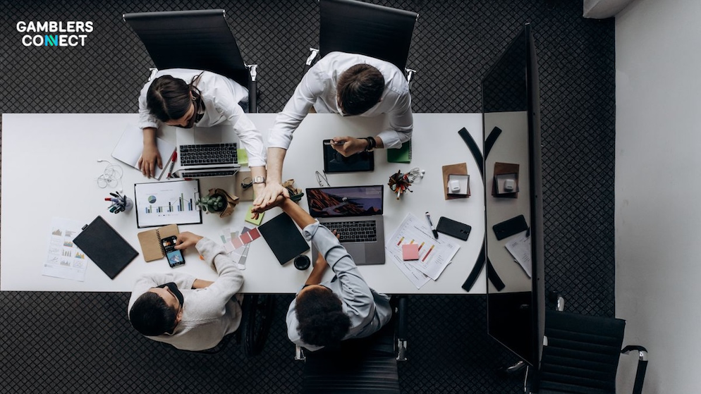 A corporate conference group executing a high-five gesture over a workspace table full of analytics documents and electronic laptops.