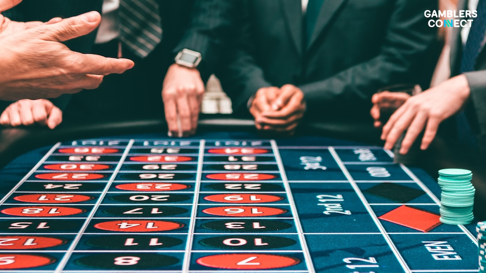 Executive patrons standing around an active casino roulette table wheel placing bets inside an upscale land-based gambling room.