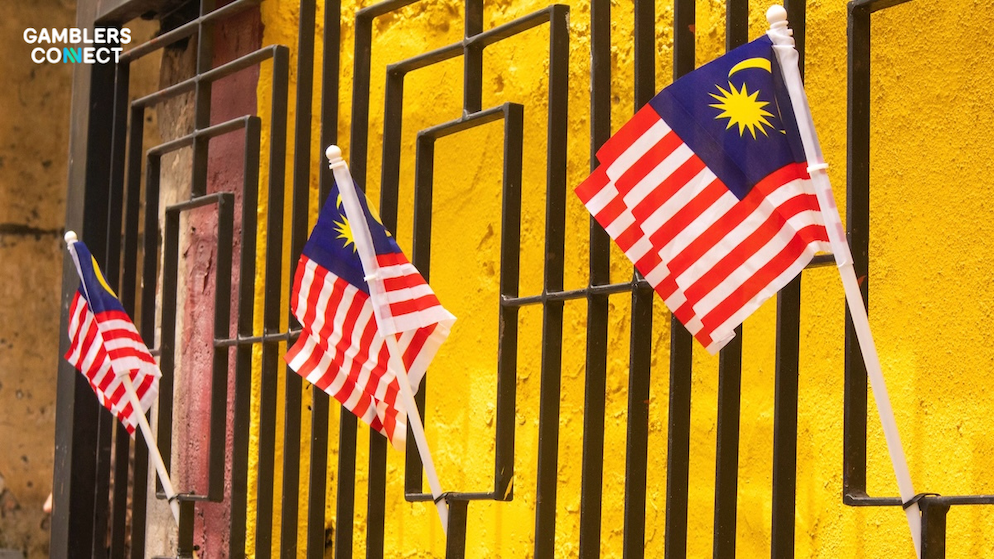 A close-up side view of small Malaysian flags attached to a black iron perimeter fence structure outside a local building facade.