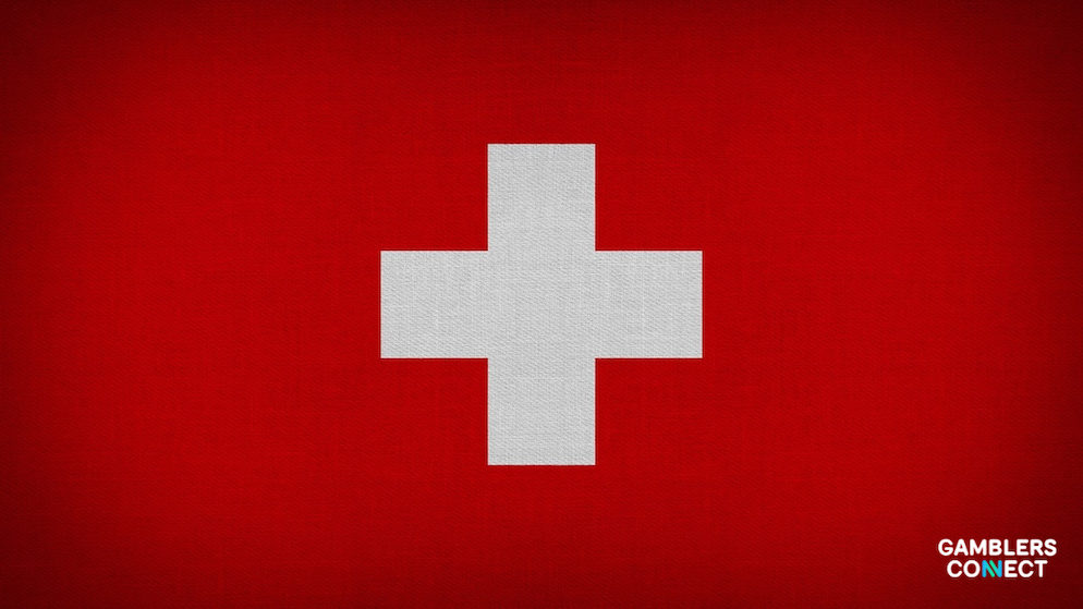 A close-up side perspective of the official red and white Swiss national flag waving in front of a neutral backdrop canvas.