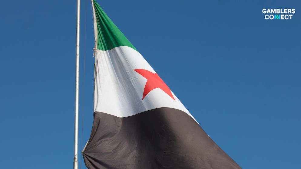 The Syrian national flag rippling smoothly under bright sunlight, representing state legal prohibitions against illegal betting applications.