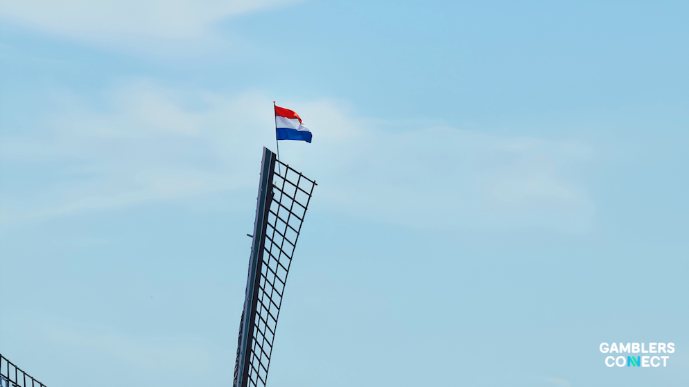The tri-color national flag of the Netherlands rippling smoothly in the wind from the highest point of a heritage windmill structure.