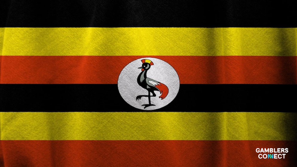 The national flag of Uganda—displaying its repeating horizontal bands of black, yellow, and red fabric with a central white circular emblem featuring a grey crowned crane bird—waving dynamically.
