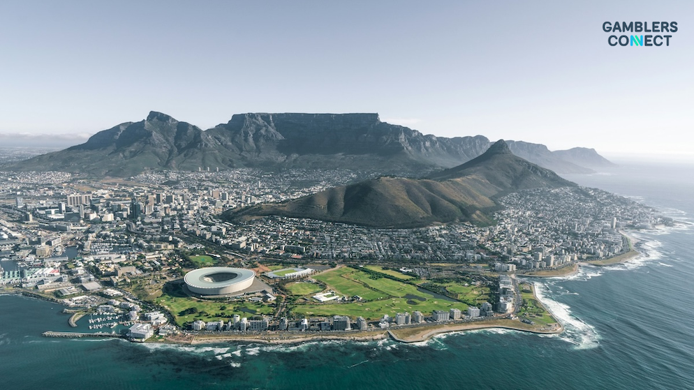 A wide daytime aerial panoramic shot of the city of Cape Town presenting the stadium and urban coastal buildings situated beneath the massive flat ridge of Table Mountain.