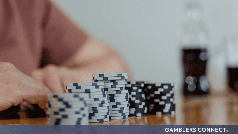 Pennsylvania Player Wins $250,000 Spin & Go Jackpot on PokerStars Exclusively on FanDuel 1 A close-up view of stacked blue, white, and black poker chips on a wooden table, with a player's hand and a soft-focused glass bottle in the background, set above a dark grey "GAMBLERS CONNECT" banner.
