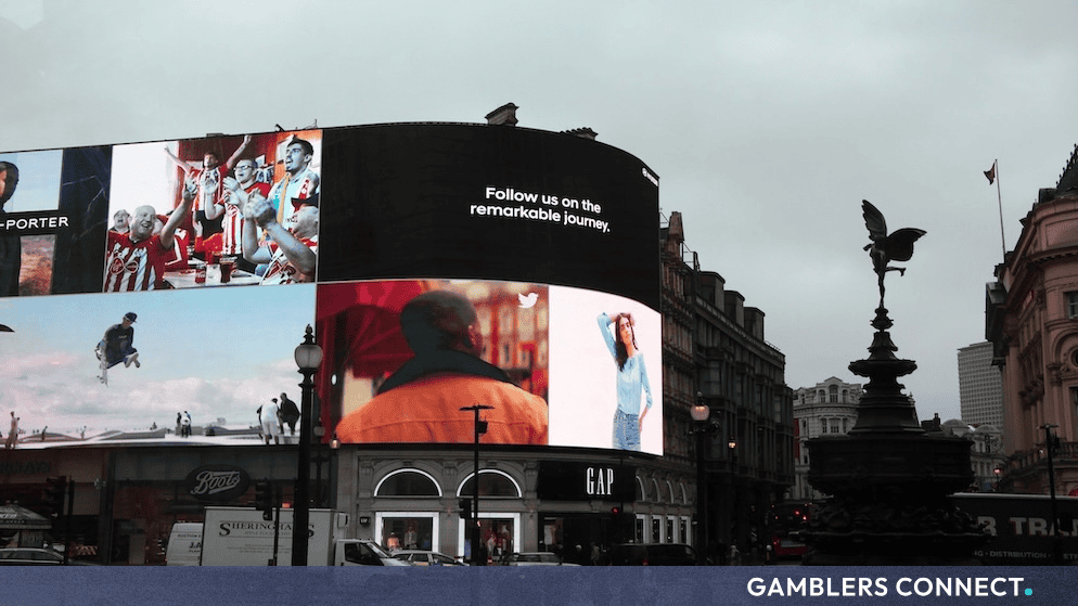 Large outdoor digital billboards displaying commercial content in a busy public square in London.