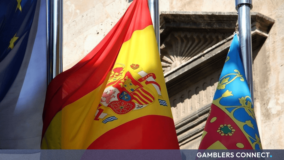 National flags of Spain and the European Union displayed outside a stone building representing regulatory frameworks and licensing.