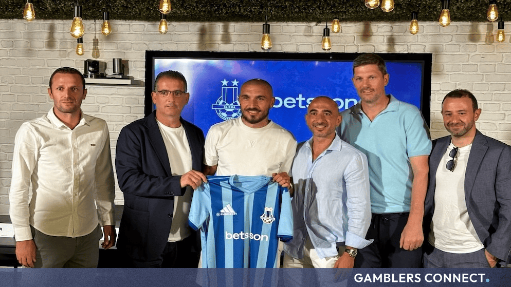 Betsson Group executives and Sliema Wanderers FC leadership posing together while holding the new light blue team jersey featuring the Betsson logo.