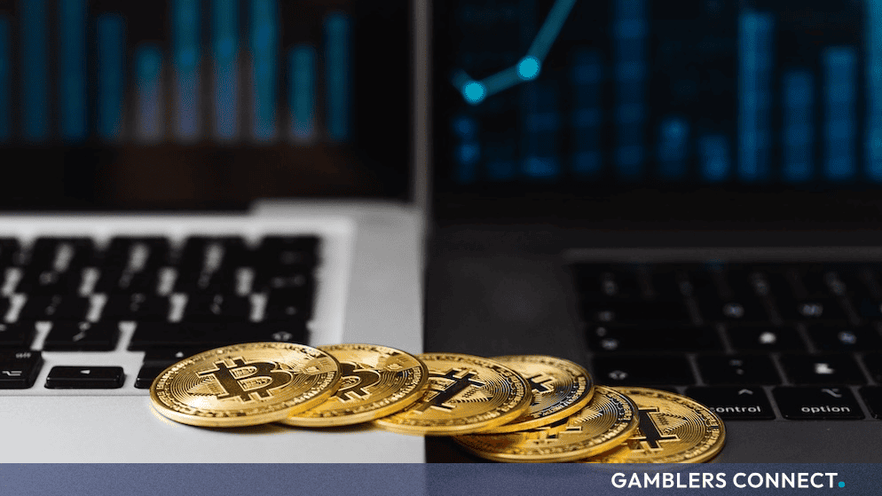 Gold Bitcoin coins sitting on a laptop keyboard with trading graphs in the background, illustrating cryptocurrency market risk adjustments.