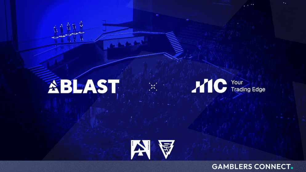 A wide view of a dimly lit, blue-themed live esports arena stage showing players standing in spotlights, with the white BLAST logo on the left and the white IC logo with the slogan 'Your Trading Edge' on the right, separated by a dotted 'X' mark.