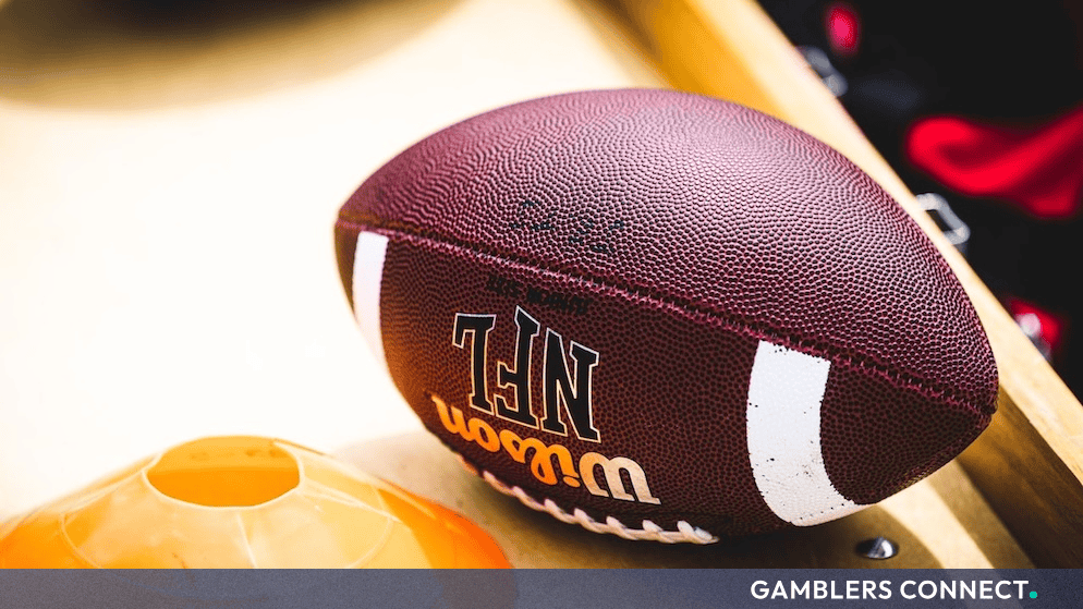 NFL Indefinitely Suspends Cardinals Executive Ryan Gold for Gambling Policy Violations 1 An official Wilson NFL leather football resting next to an orange practice cone on a wooden sideline bench.