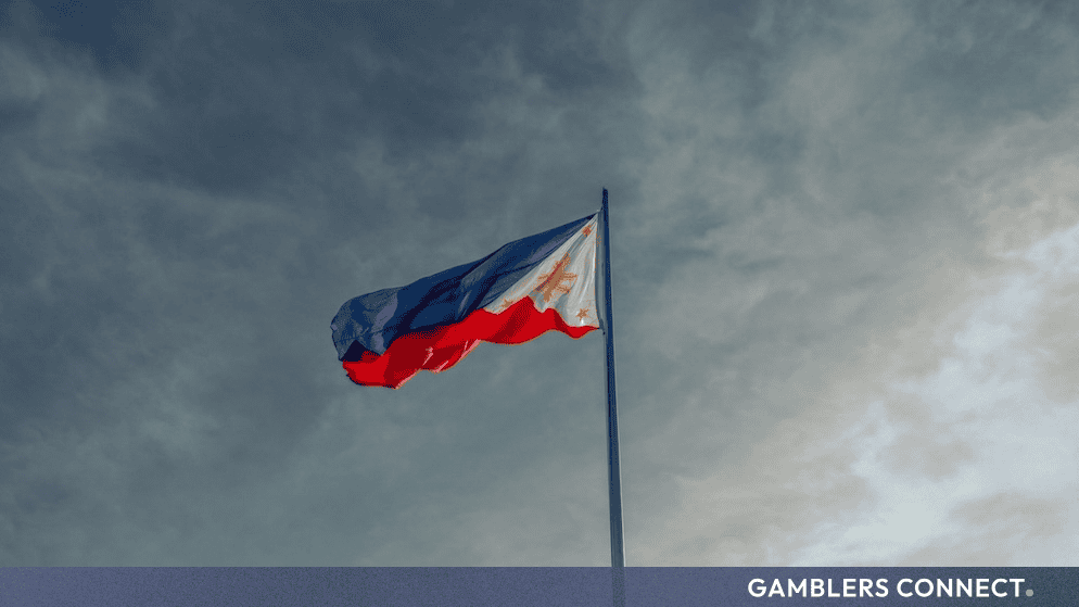 The national flag of the Philippines waving from a tall metal pole against a dramatic, cloudy sky.