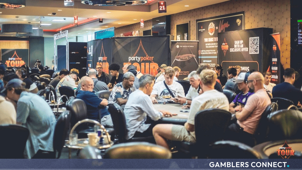 Live poker players seated at card tables with orange and black PartyPoker Tour branding banners visible in the background background.