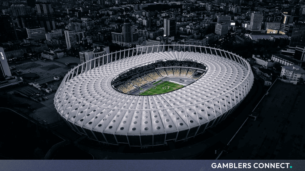 Aerial view of a large illuminated football stadium at dusk, surrounded by a cityscape.
