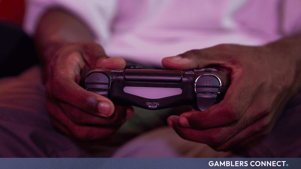 A close-up view of a person holding a game controller while playing a video game in a dimly lit room.