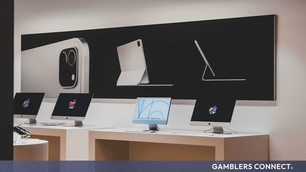 Interior view of an Apple retail store displaying various Mac computers and promotional graphics on the wall.