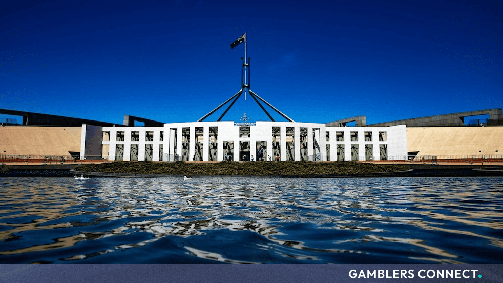 The exterior facade of Australian Parliament House in Canberra reflected in the waters of front pool under a clear blue sky.