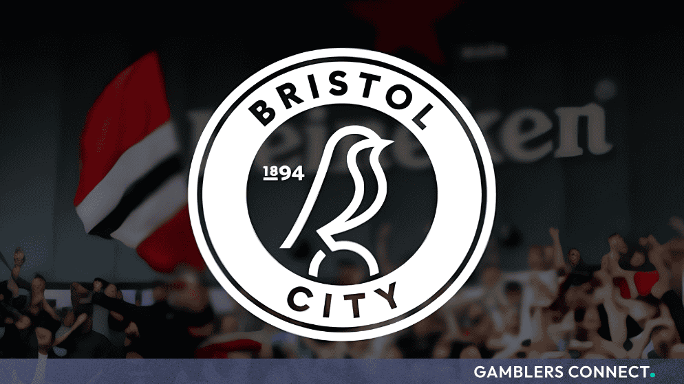 The official club crest of Bristol City Football Club displayed prominently against a blurred background of fans at Ashton Gate Stadium.