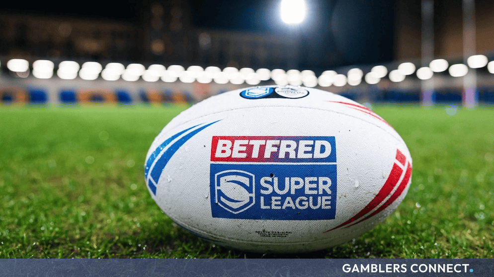 A rugby league ball featuring the Betfred Super League logo resting on the pitch at a stadium.
