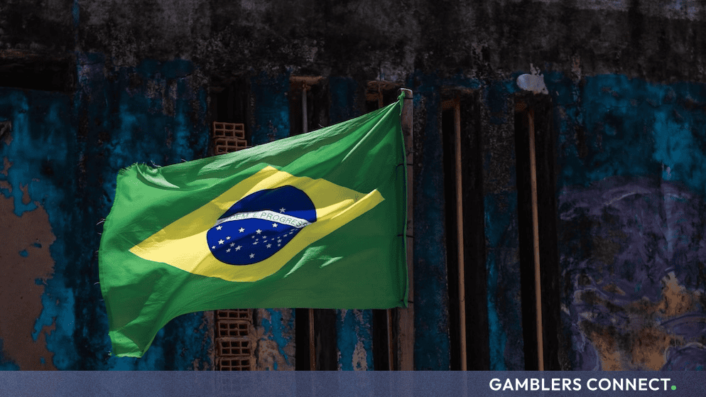 The national flag of Brazil waving outdoors against a weathered blue wall.