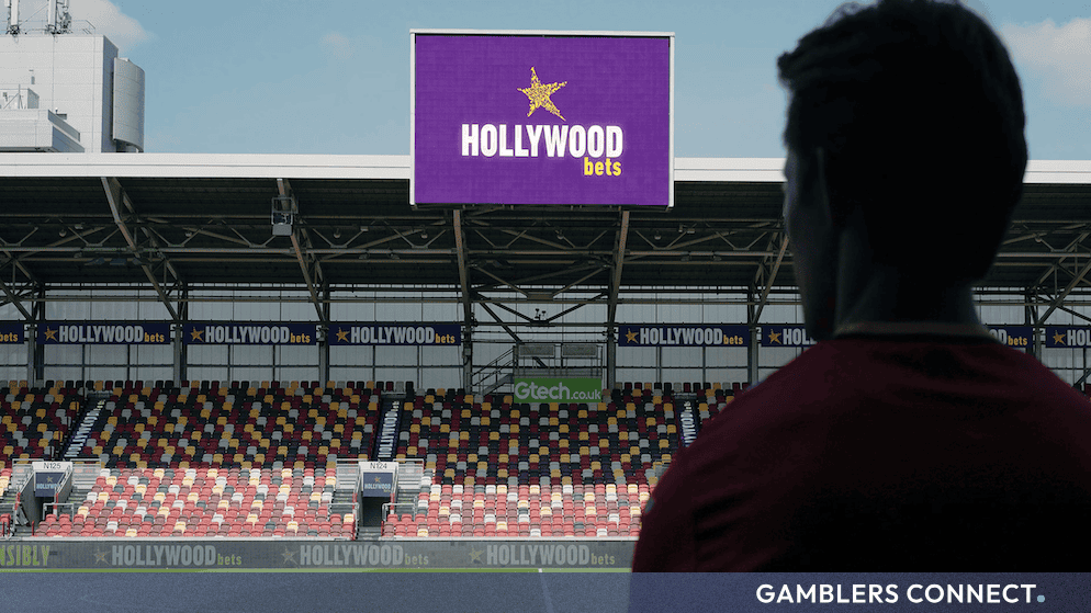 View from the pitch looking up at the large stadium screen and stands featuring Hollywoodbets branding at Gtech Community Stadium.