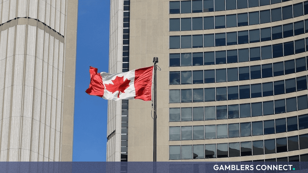 The national flag of Canada waving proudly in front of a modern high-rise urban corporate building.