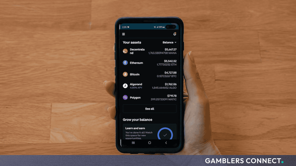 A person holding a smartphone displaying an asset portfolio interface against a wooden tabletop.