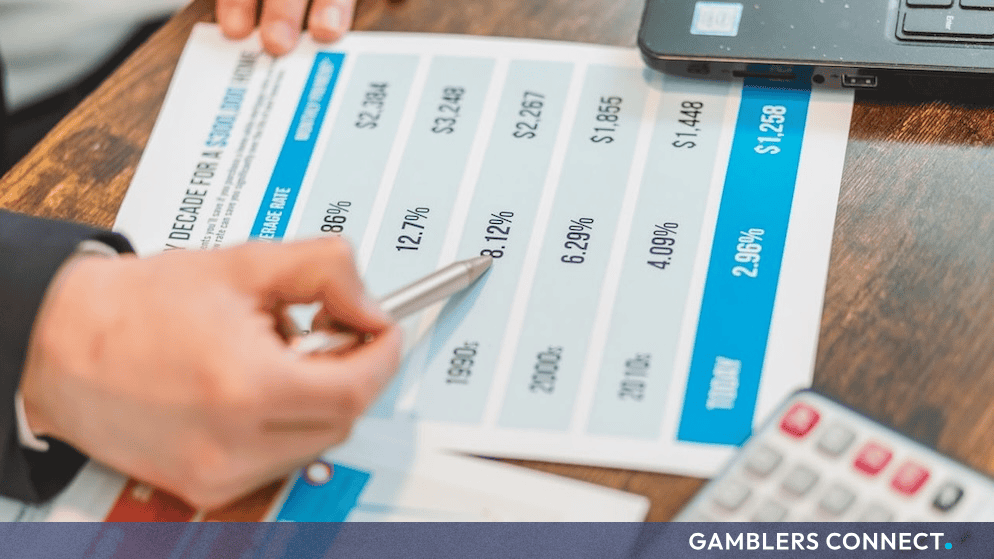 A financial analyst reviewing data charts and financial projections with a calculator and laptop on a wooden desk.