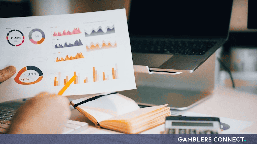 A person reviewing analytical charts and statistical data sheets alongside a laptop and calculator, representing research on youth gambling behavior.