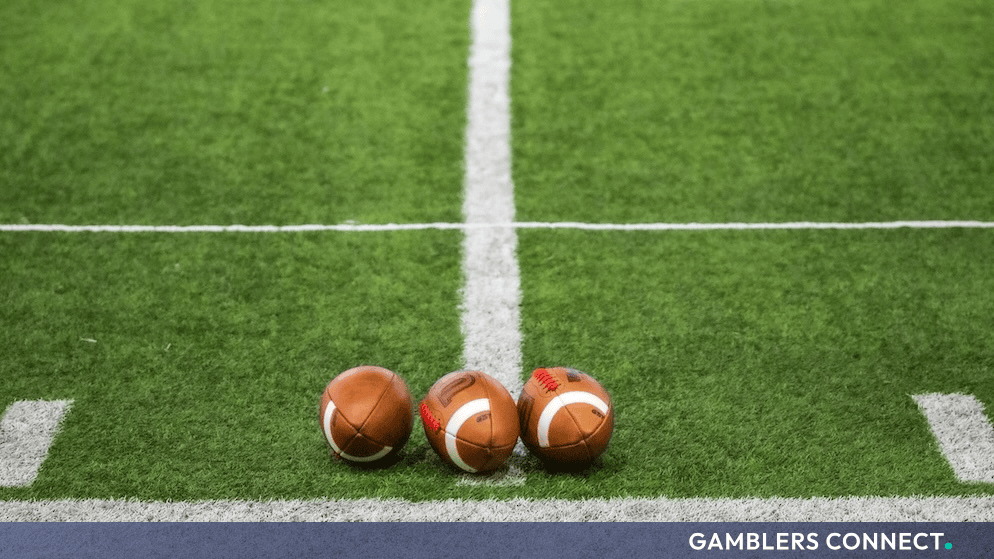 Three regulation footballs resting on a neatly mown green turf field marked with white yard lines.