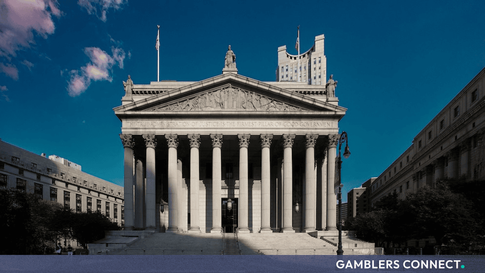 A grand neoclassical courthouse building featuring towering stone columns and detailed architectural relief under a bright blue sky.