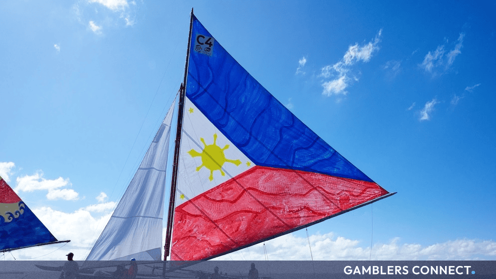 A traditional sailboat featuring the Philippine national flag sailing on open blue water under a partly cloudy sky.