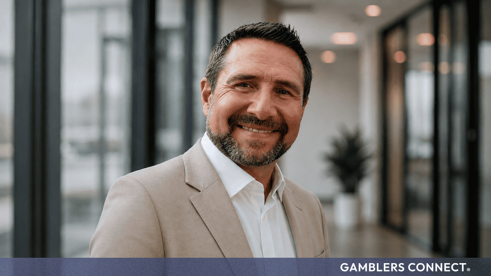 Professional headshot of Phil Walker, newly appointed interim CEO of Allwyn UK, smiling in a tailored beige jacket and crisp white shirt.