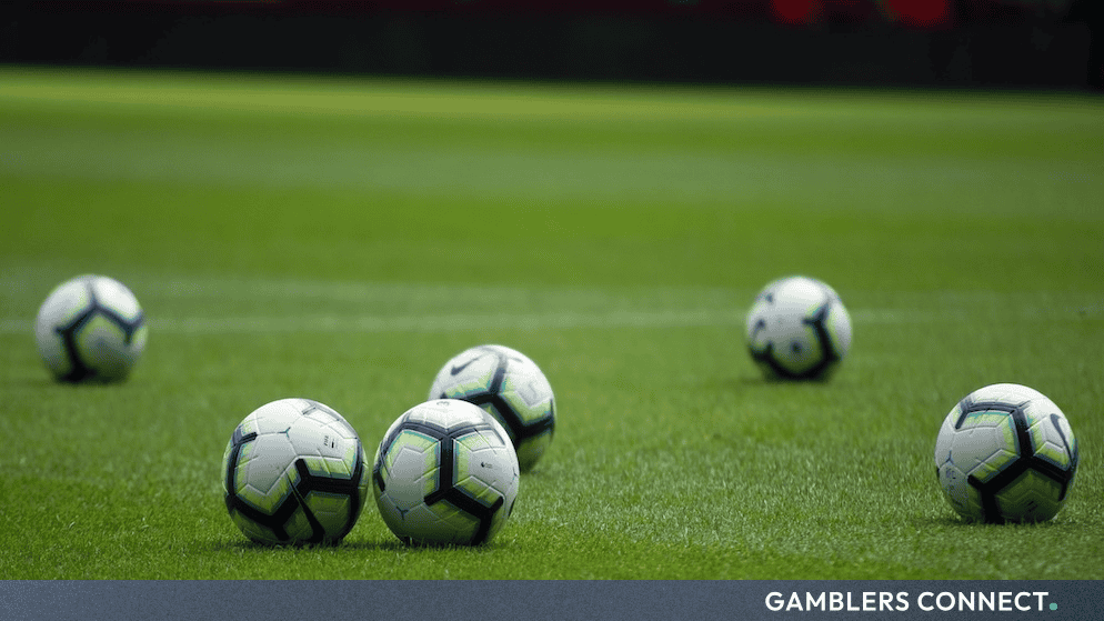 Several white and blue footballs resting neatly on lush green pitch turf during a professional match.