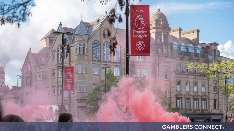 Street decorated with Premier League banners and pink smoke during a football match day celebration.