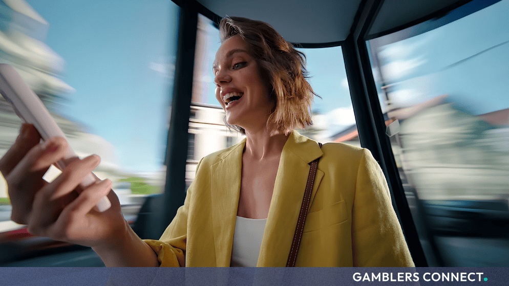 A smiling woman holding her smartphone inside a dynamic, fast-moving vehicle setting for the DraftKings Casino campaign.