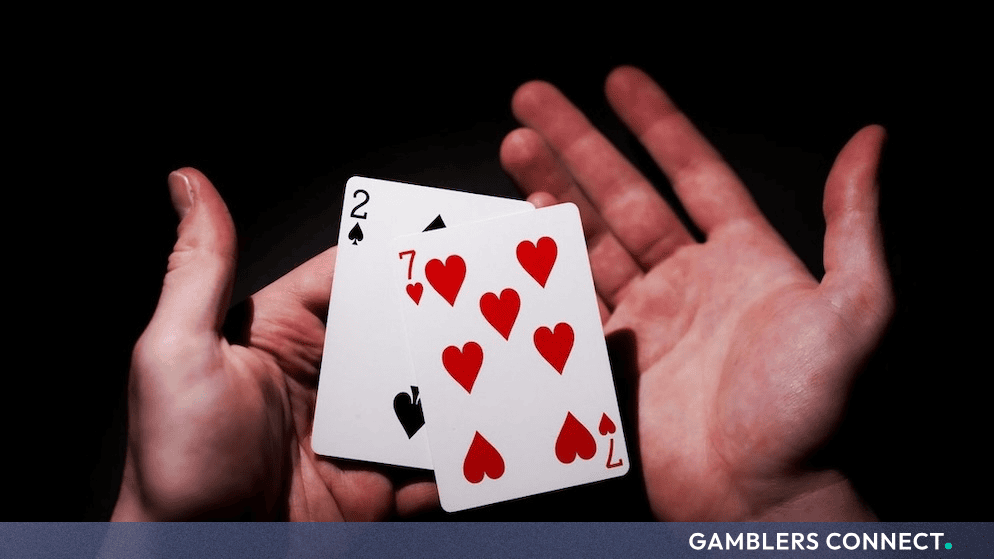 A pair of playing cards held in hands against a dark background, symbolizing the risks and challenges of problem gambling.