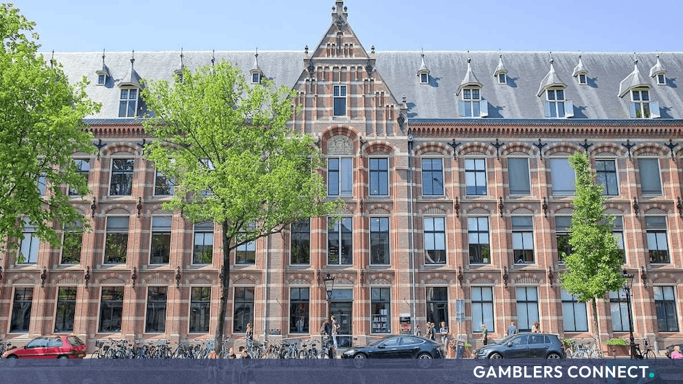Classic historical brick architecture of a University of Amsterdam building alongside a canal with parked bicycles and cars.