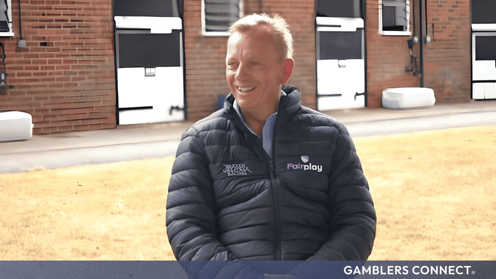 Trainer Warren Greatrex wearing a Fairplay-branded jacket while standing outside stable yards at his Lambourn training base.
