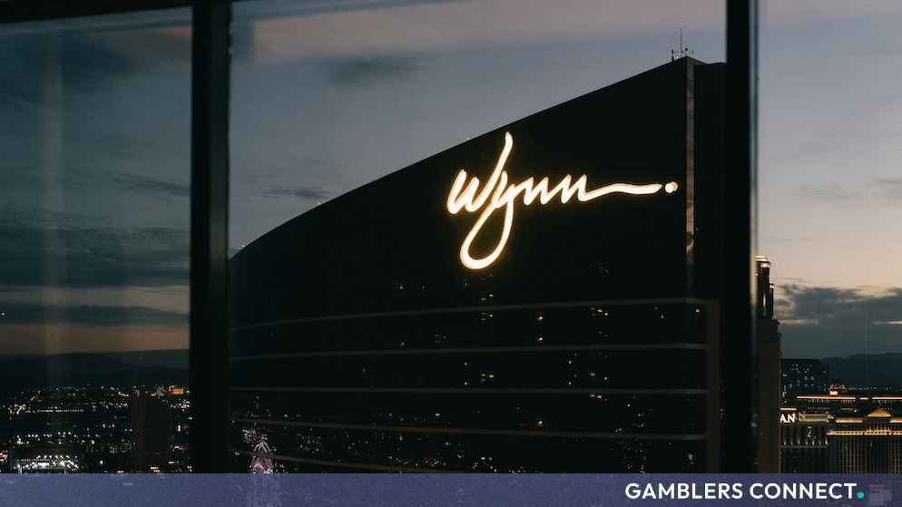 Exterior architectural view of the illuminated Wynn resort tower against an evening sky.