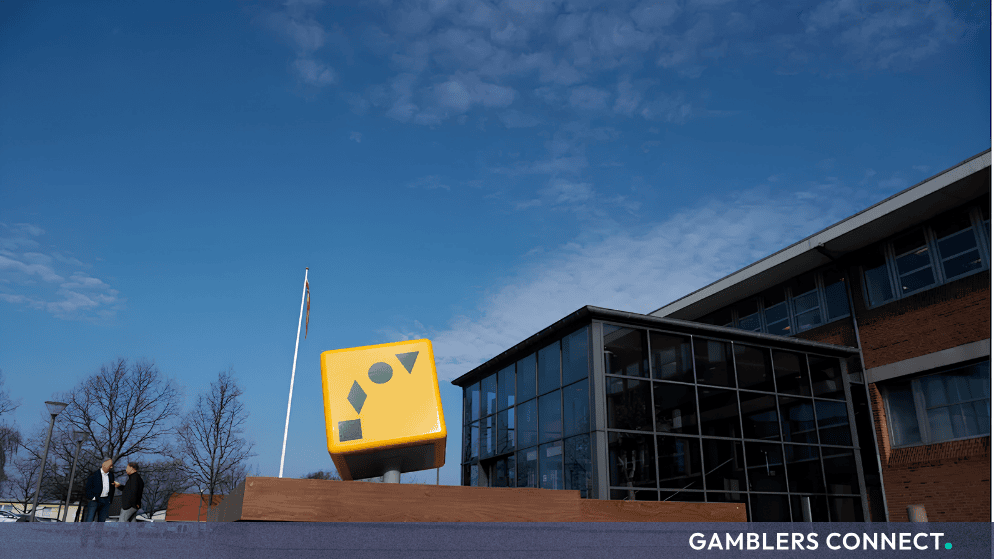 Exterior view of the Danske Spil headquarters featuring a distinctive yellow cube logo against a clear blue sky.