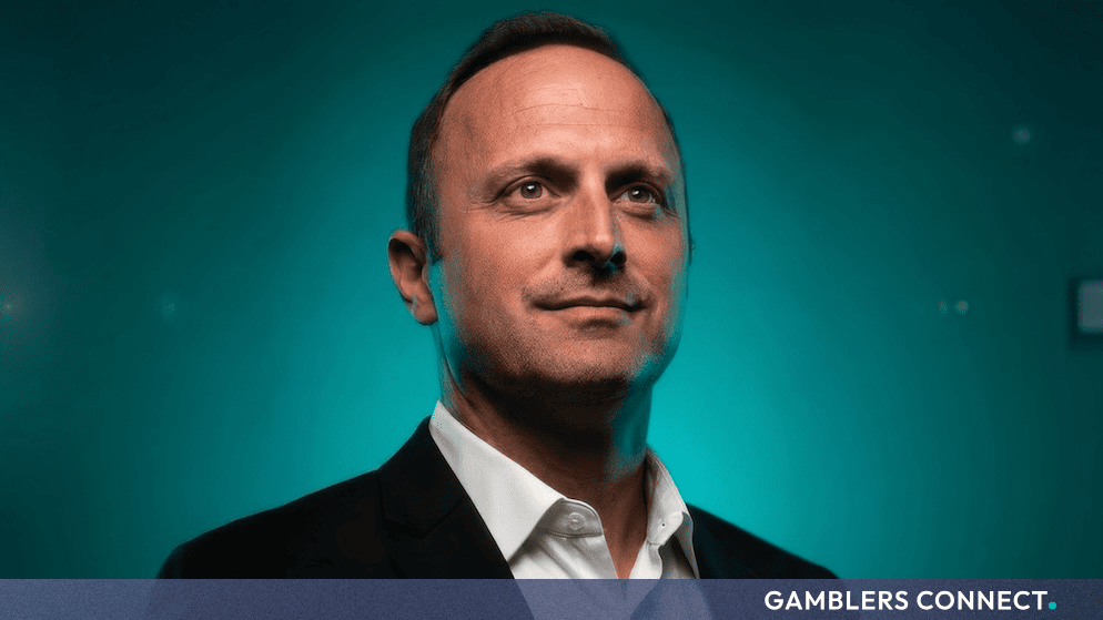 Professional portrait of Drew M. Kelley, Chief Executive Officer of BTG977, wearing a dark suit jacket and white collared shirt against a teal background.