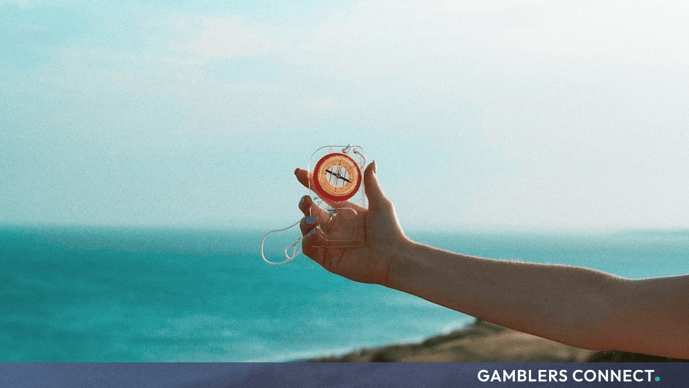 A hand holding a transparent compass outdoors with a scenic coastal and ocean background.