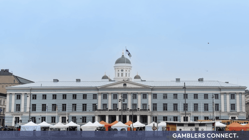 Historic government building in Helsinki, Finland, under a clear sky with market tents in the foreground.