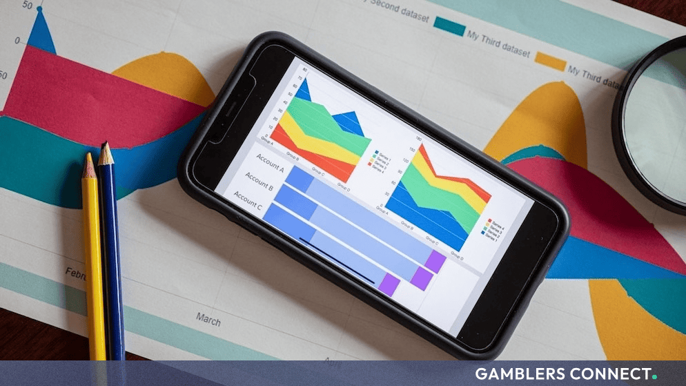 A smartphone displaying colorful data charts and analytics resting on top of printed financial graphs accompanied by pencils.