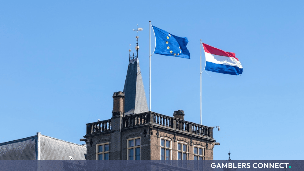 The flags of the European Union and the Netherlands flying proudly atop a historic European building against a clear blue sky.