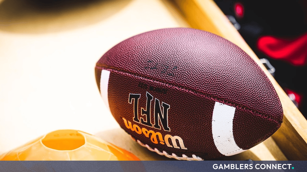 An official NFL football resting on a wooden surface beside an orange training cone.
