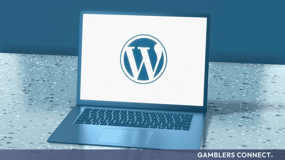 A modern blue laptop displaying the official WordPress logo on its screen against a speckled surface.