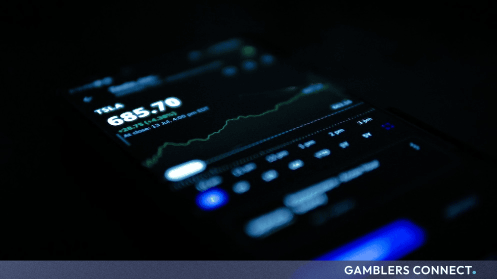 A mobile phone screen displaying financial market graphs and stock trading data in a dark room.