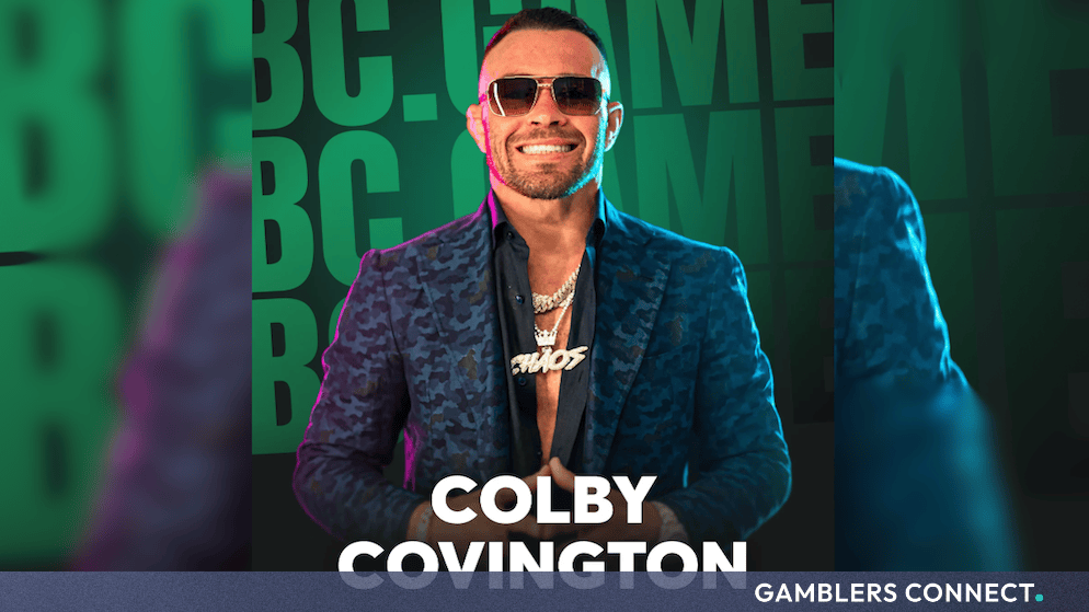 Colby Covington wearing sunglasses and a patterned blazer smiling against green BC Game promotional branding